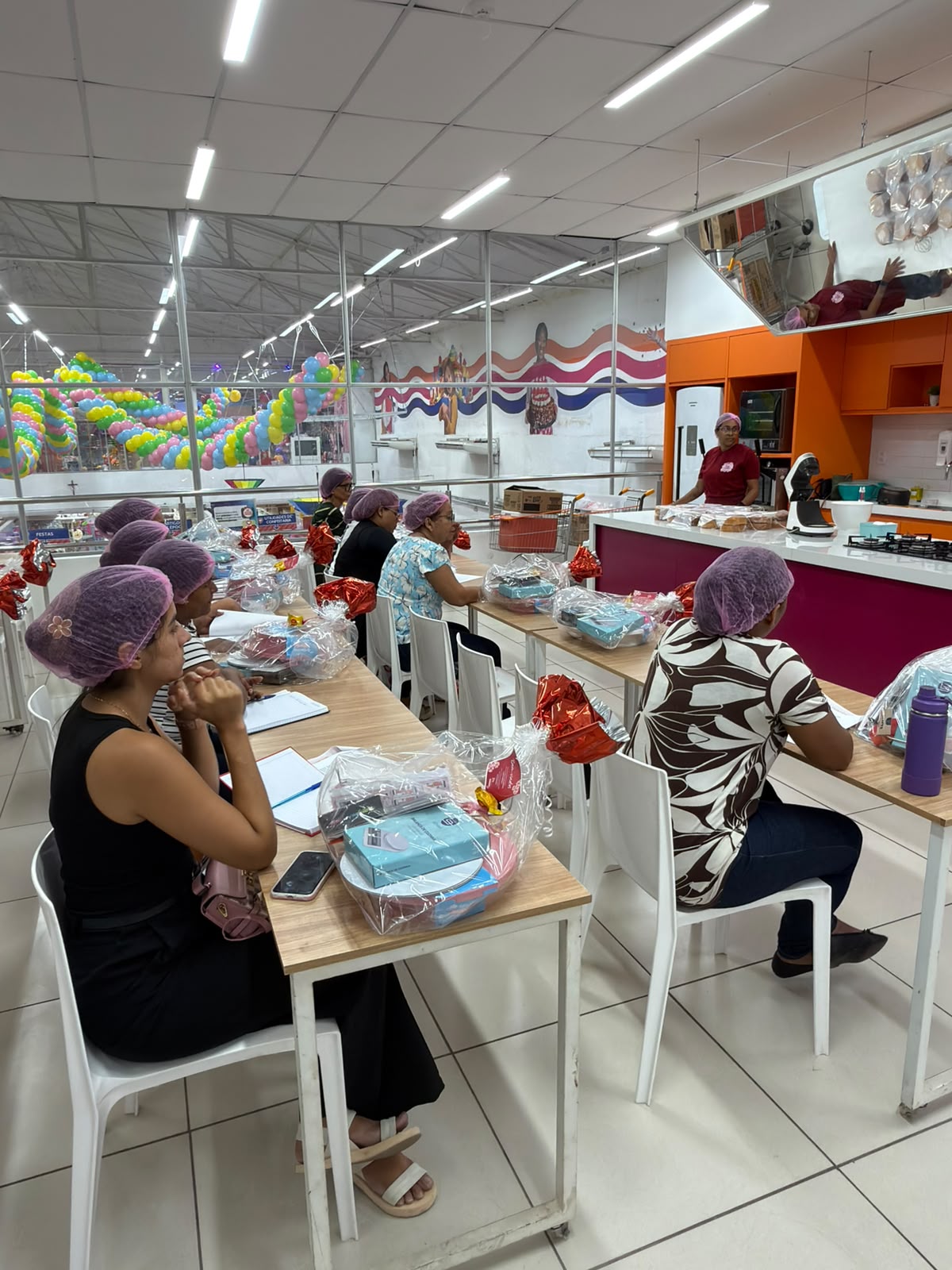 Mulheres participam de capacitação em Confeitaria do projeto Profissionalizar para o Futuro, com kits de materiais sobre as mesas.